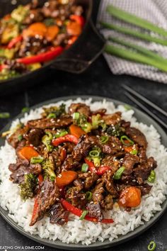 beef and vegetable stir fry served over rice on a black plate with chopsticks