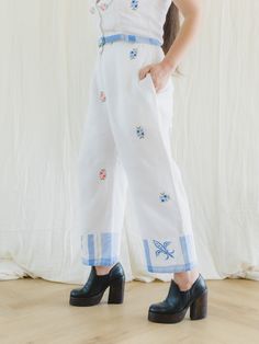 Introducing our stunning and one-of-a-kind Crop Top and Pants Set! Made from various vintage textiles, this exquisite set features vibrant and colorful hand embroidery in various floral designs, adding a unique touch to your wardrobe. The sleeveless crop top has an even hemline and lace detailing, perfect for a summer day.   The high waist pants come in a beautiful white color and have elastic on the waist at the sides with one button at the front for a flawless fit. The cotton fabric is adorned with subtle floral embroidery and has pockets on both sides, adding both style and functionality to the set.    One-of-a-kind upcycled vintage top and pants Top closes with 4 buttons down the front.  Pant has 8" zippers at the front with a button Fabric: Linen/ Cotton   Care: Machine wash with cool Blue Embroidered Spring Pants, Traditional Spring Sets With Embroidered Hem, Traditional Sets With Embroidered Hem For Spring, Blue Floral Embroidered Wide Leg Bottoms, Blue Cotton Bottoms With Embroidered Hem, Spring Wide-leg Pants With Floral Embroidery, Fitted Cotton Pants With Chikankari Embroidery, Spring Cotton Embroidered Bottoms, Blue Floral Embroidered Pants For Summer