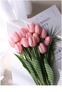 a bouquet of pink tulips sitting on top of a white table next to an envelope