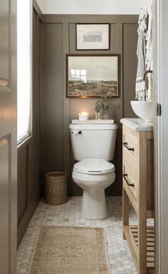 a white toilet sitting inside of a bathroom next to a wooden cabinet and sink under a mirror