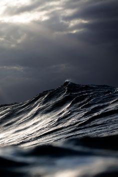 black and white photograph of ocean waves with sun shining through clouds in the sky above