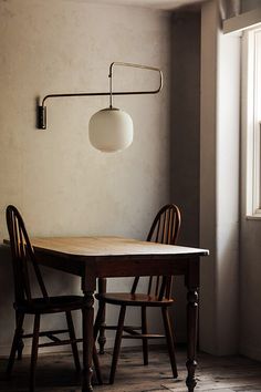 a table and two chairs in front of a window with a lamp on the wall