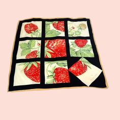 a quilted table cloth with strawberries and leaves on black fabric, in front of a pink background