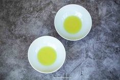 two white bowls filled with green liquid on top of a table