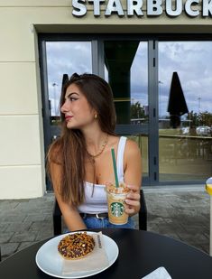 a woman sitting at a table in front of a starbucks drink with a donut