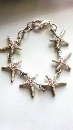 Most of our work revolves around the beach, sand, and sun. Have you ever held a starfish? They are super awesome and wiggle when held. We've always been fascinated by these wonderful sea creatures! Our bracelet features wonderful starfish about one inch in size with cute rhinestones in them. They really catch the light and would look great for your online meetings! We added extra links and a nice size lobster claw closure-cause we hate those tiny ones! This bracelet easily adjusts 7 to 8 inches Cheap Bracelets With Starfish Charm For Gift, Affordable White Charm Bracelet For Beach, Silver Starfish Jewelry For Beach, Silver Starfish Jewelry For Vacation, Beach Jewelry With Starfish Charm, Beach Adjustable Jewelry With Star Charm, Beach Jewelry With Adjustable Star Charm, Adjustable Beach Jewelry With Star Charm, Adjustable Starfish Bracelet With Lobster Clasp