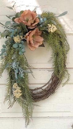 a wreath is hanging on the side of a white door with greenery and flowers