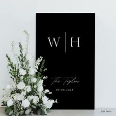 white flowers and greenery sit in front of a black sign that reads wh