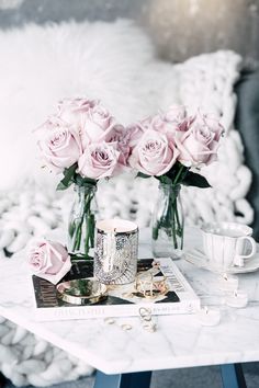 pink roses in vases sitting on top of a table next to a cup and saucer