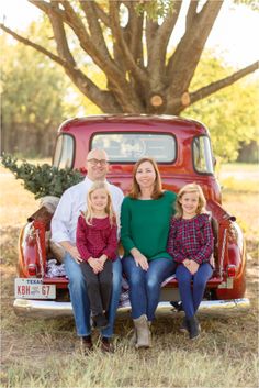 a family sitting on the back of an old red truck in front of a tree