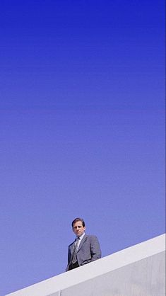 a man in a suit standing on top of a white wall and looking up at the sky