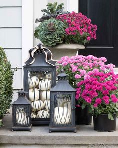 three lanterns are sitting on the steps with flowers in front of them and one is filled with white pumpkins