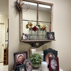 a table with pictures and vases on it in front of a mirror that is hanging from the wall