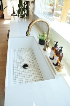 a white sink sitting under a window next to a counter top with soap and lotion