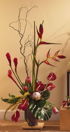 a vase filled with red flowers sitting on top of a wooden table next to a wall