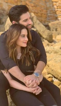 a man and woman sitting on rocks holding hands