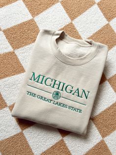 Michigan, the Great Lakes State with a lake scene doodle. The emerald green thread pops against the neutral sand crew color! Brand: Gildan, unisex fit Lake Scene, Green Thread, The Great Lakes, Embroidered Tee, Embroidery Sweatshirt, Embroidered Crewneck, Embroidered Hoodie, College Student, Crew Neck Shirt