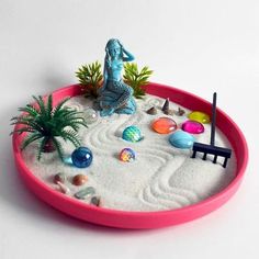 a pink tray with sand, plants and rocks in it on a white table top