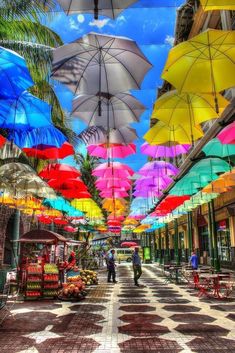 many colorful umbrellas are hanging in the air above an open market area with checkered flooring