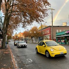 a yellow car driving down a street next to a tree with a rainbow in the background