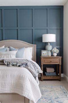 a bedroom with blue paneled walls and a white bed in the corner, along with a nightstand