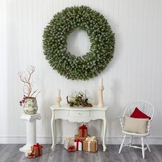 a christmas wreath on the wall next to a table with presents and a white chair