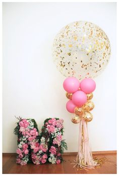 balloons and flowers are sitting on the floor next to the letter m, with one balloon in the air