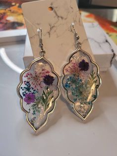 a pair of earrings with flowers painted on the front and back of them, sitting on top of a marble table