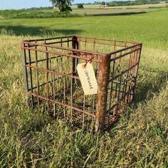 an old rusted metal cage in the middle of a field with a sign on it