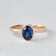 a gold ring with a blue sapphire stone on the front and side, sitting on a white surface