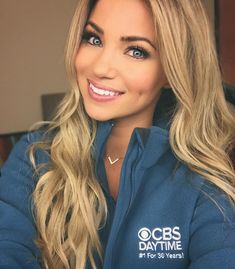 a woman with long blonde hair wearing a blue hoodie and smiling at the camera