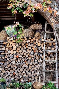 a pile of logs sitting next to a building with baskets on top of it and plants in the background