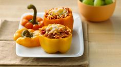 three stuffed bell peppers on a white plate with other food items in the back ground