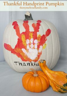 a handprinted pumpkin sitting next to an orange and white pumpkin with the word thank you written on it