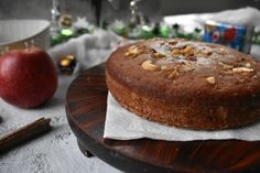 a cake sitting on top of a wooden plate next to an apple and cinnamon stick