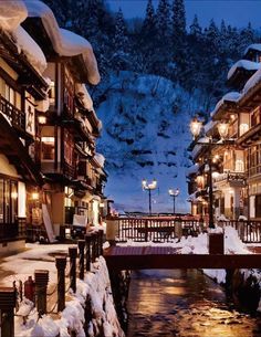 a river running through a snow covered street next to tall buildings with lights on them