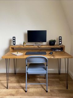 a wooden desk with two chairs and a computer monitor on it, in front of a white wall