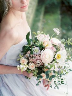 a woman in a white dress holding a bouquet of flowers and greenery on her wedding day