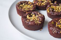 several chocolate muffins on a white plate topped with nuts