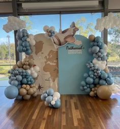 an arch made out of balloons and other items on a wooden floor in front of a window