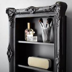 an ornate black shelf with makeup brushes and other items on it in front of a white wall