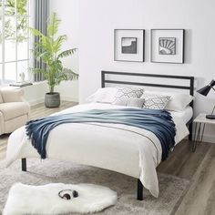 a bedroom with white walls and wood flooring has a large bed, two chairs, and a rug on the floor