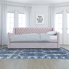 a pink couch sitting on top of a rug in a living room next to windows