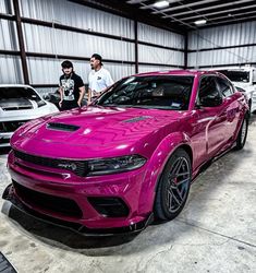 two men standing next to a pink car in a garage