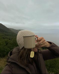 a woman holding a cup with a tag on it while standing in front of the ocean