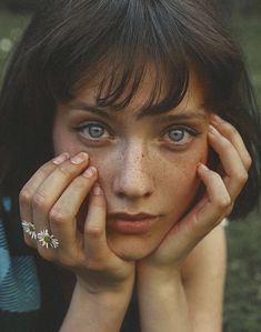 a young woman with freckles on her face and hands resting against her cheek