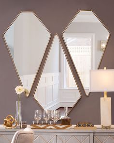 two mirrors on the wall above a dresser with a lamp and vase in front of it