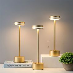 three gold colored lamps sitting on top of a white table next to a potted plant