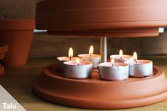 several lit candles sitting on top of a brown stand next to some potted plants