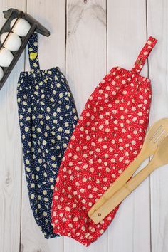 two aprons with wooden utensils next to them on a white wood surface